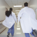Rear view of doctors running down corridor in hospital