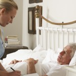 Nurse Visiting Senior Male Patient In Bed At Home