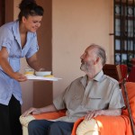 nurse or helper in residential home giving food to senior man