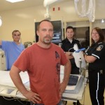 Tom Halloway stands in the room where he was operated on after his heart attack. Behind to the left is Dr Dominic Rocco, chief of cardiology who performed the procedure of installing a stint and on the right two EMS staff Mathew Galicia and Jennifer Evans similar to the team that responded to Tom’s emergency.