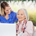 Happy Granddaughter With Senior Woman Using Laptop On Porch