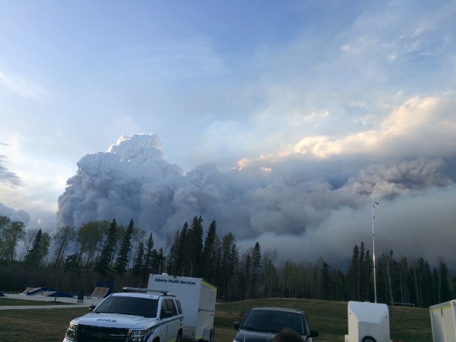 Wildfire smoke billows up behind an AHS EMS unit. EMS crews remained a constant presence throughout the evacuation, to provide support as needed.